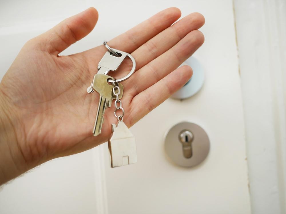 une main tenant un trousseau de clé devant une porte 
