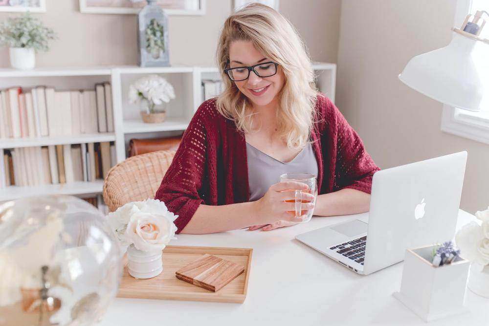 une femme à son bureau devant un ordinateur avec un thé dans la main