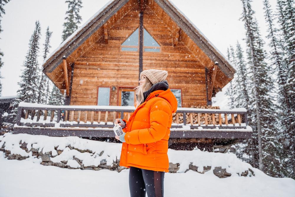 un chalet morderne dans la neige avec une femme en veste de ski orange