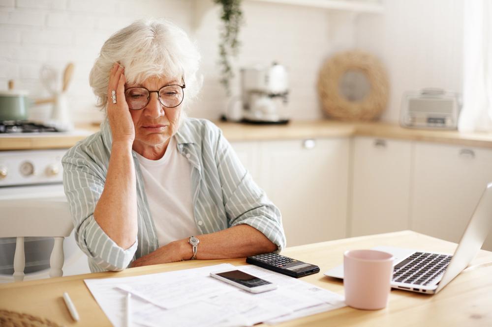une dame cheveux grisonnant devant des papiers et faisant des calculs